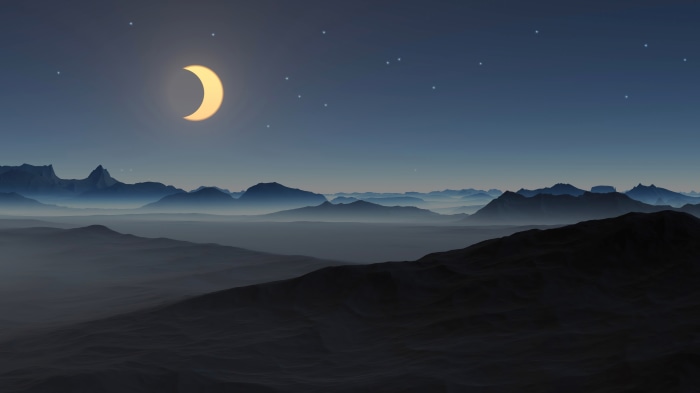 Crescent moon over misty mountains at night
