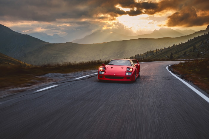 Red Ferrari F40 driving on mountain road at sunset