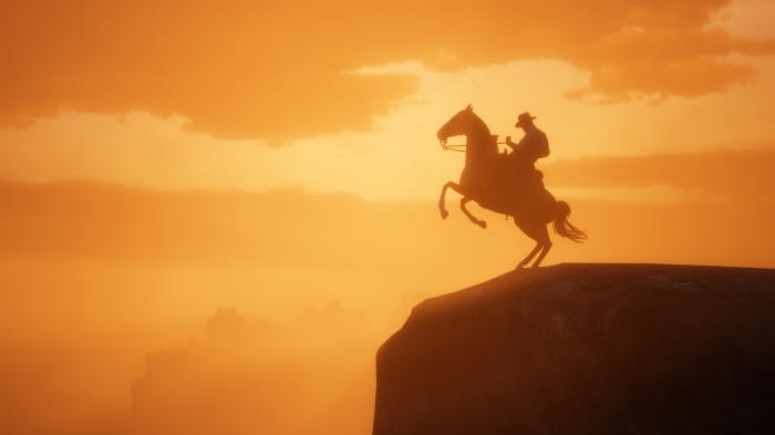 Cowboy on a horse rearing on a cliff at sunset