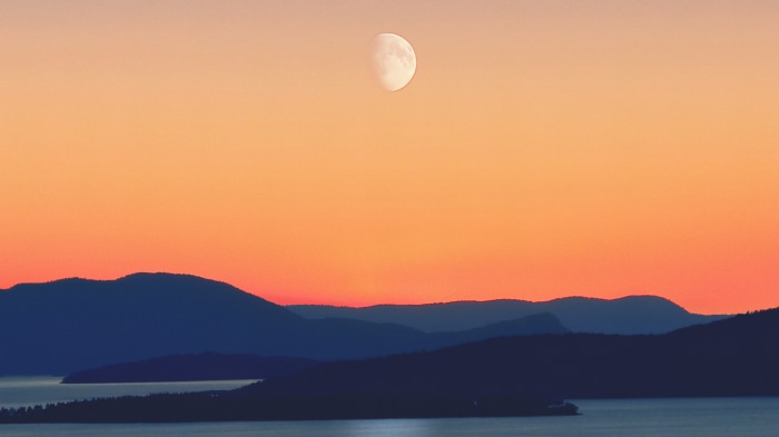 Moon over silhouetted mountains and water at sunset