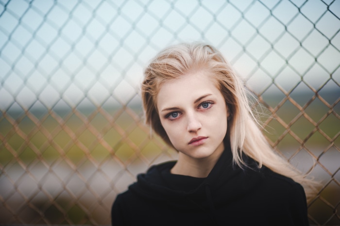 Blonde girl in black hoodie behind fence