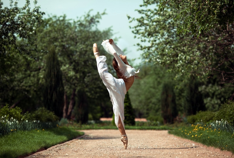 Ballerina in white performs a split in a park