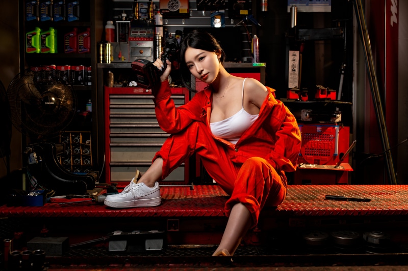 Asian woman in orange jumpsuit holding a tool