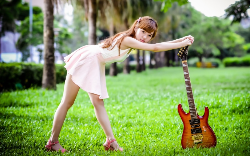 Asian girl in pink skirt with guitar in park