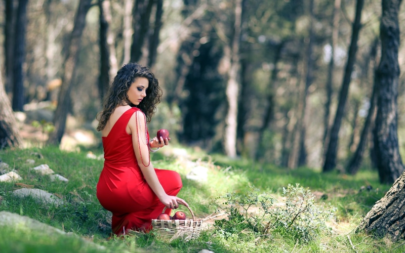 Brunette girl in red dress holding an apple in a forest
