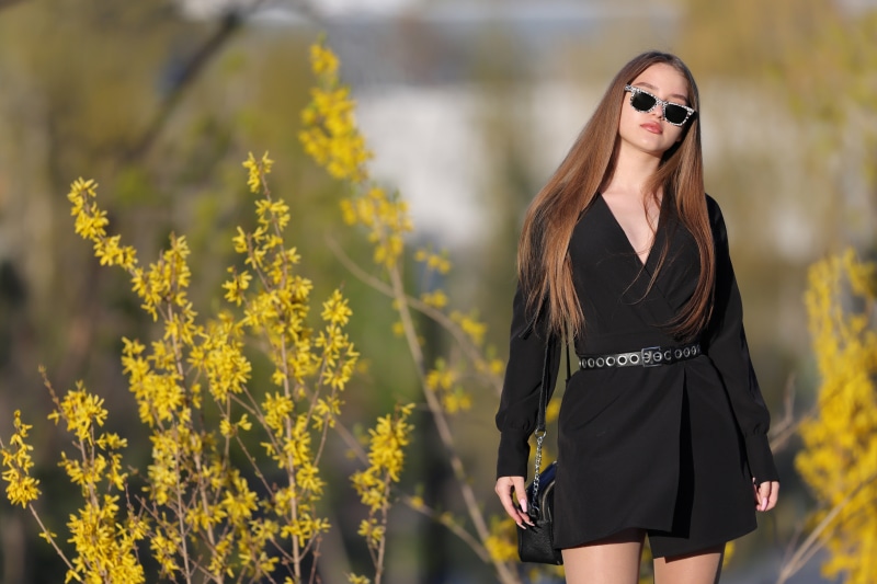 Woman with sunglasses and black dress near yellow flowers
