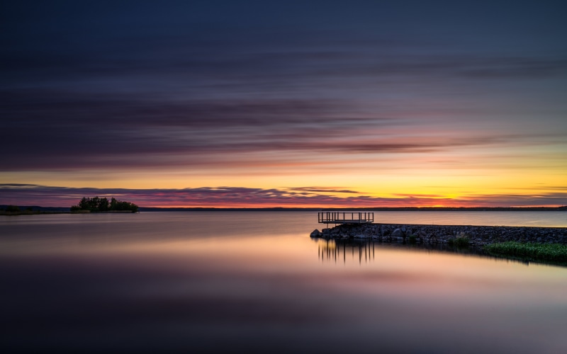 Sunset over a calm lake with a small island and pier