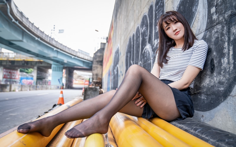 Asian girl in pantyhose sitting by graffiti wall