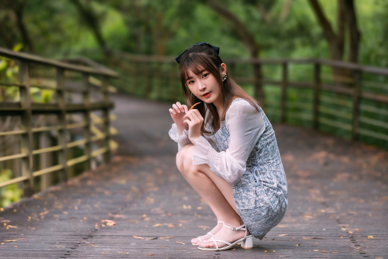 Asian woman in dress crouching on a wooden bridge
