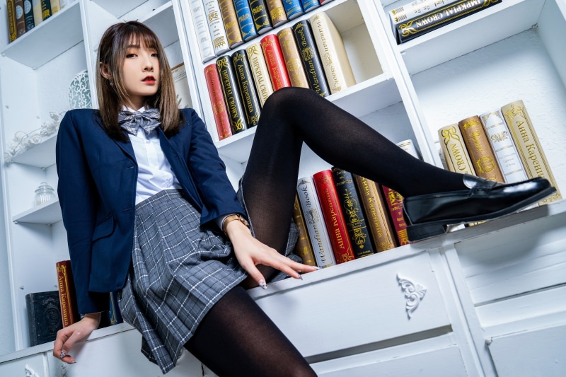 Asian girl in school uniform sitting on bookshelf