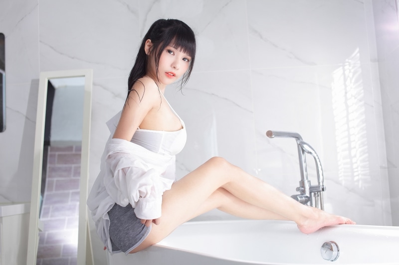 Asian girl in bathroom sitting on bathtub edge