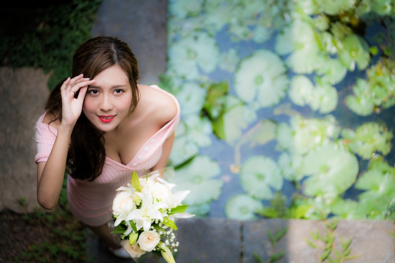 Asian woman in pink dress holding bouquet near pond