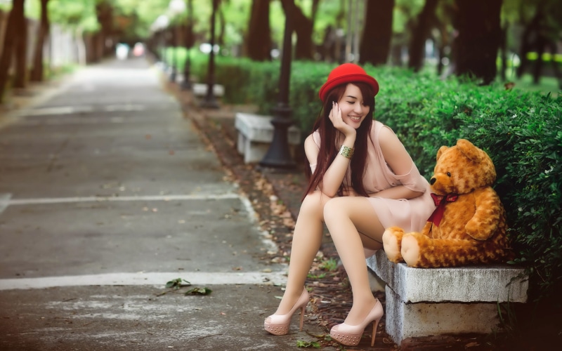 Brunette girl in red hat with teddy bear in park