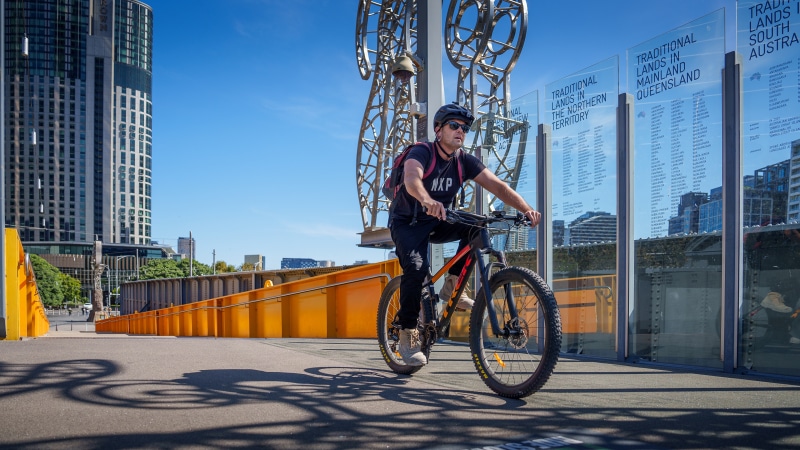 Man riding bicycle past traditional lands display in Melbourne
