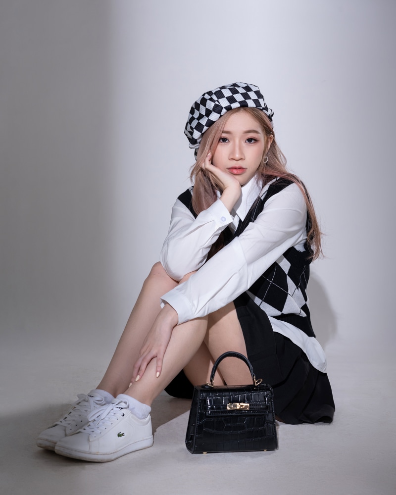 Asian woman wearing beret and vest, sitting with handbag