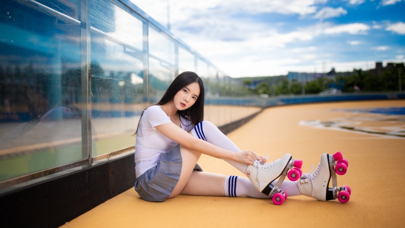 Brunette girl with roller skates sitting on a court