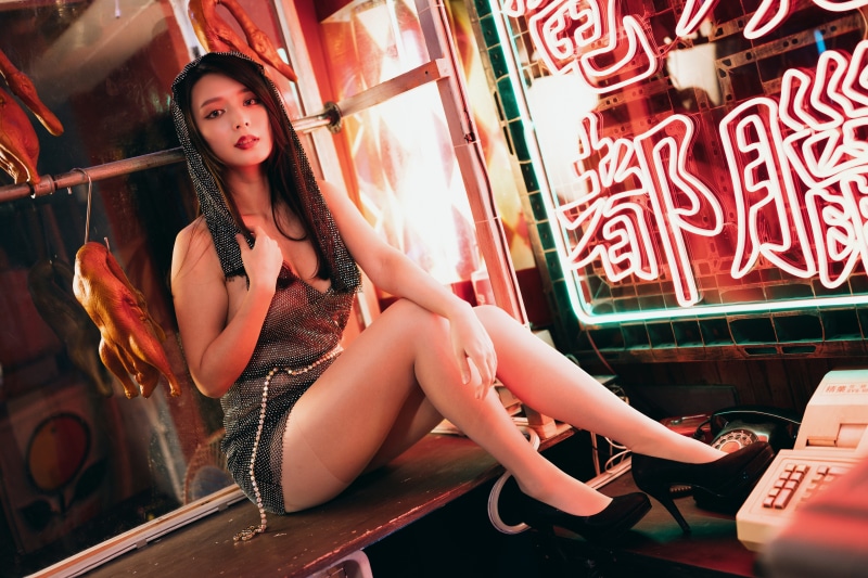 Asian woman in dress sitting near neon signs