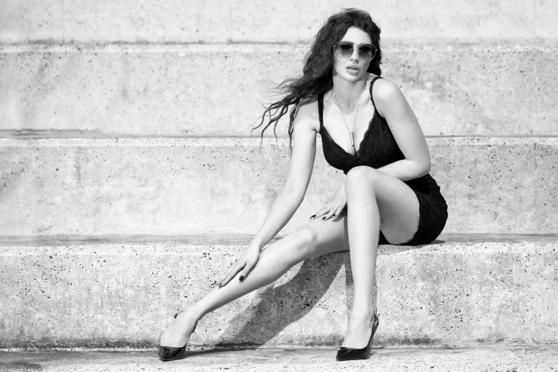 Karina in a black dress and sunglasses sitting on steps