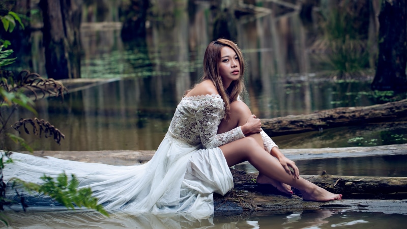 Woman in white dress sitting on a log in water