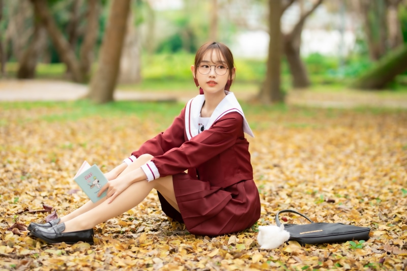 Asian schoolgirl with glasses reading a book in autumn foliage