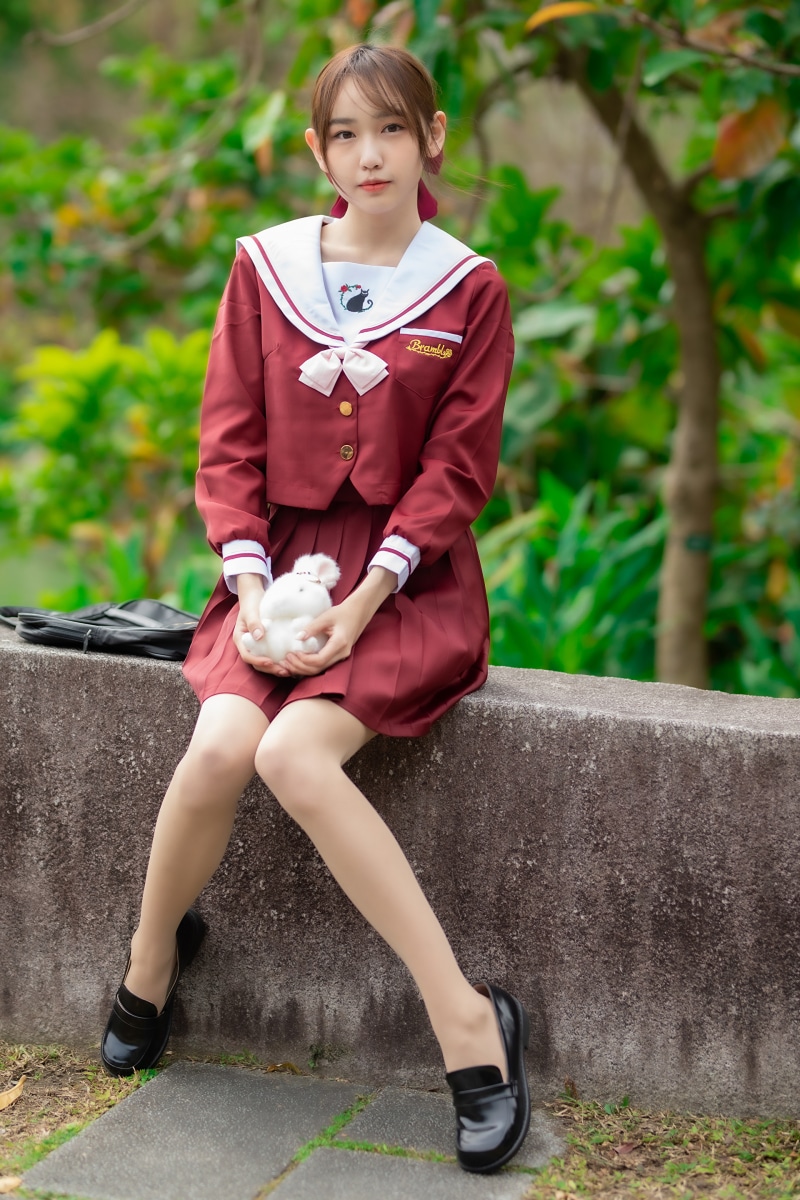 Asian schoolgirl sitting outdoors holding a stuffed animal