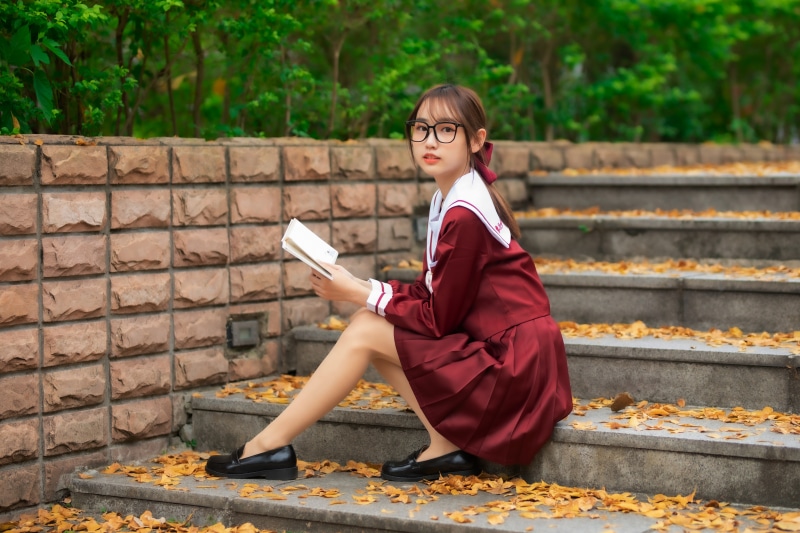 Asian schoolgirl sitting on steps reading a book