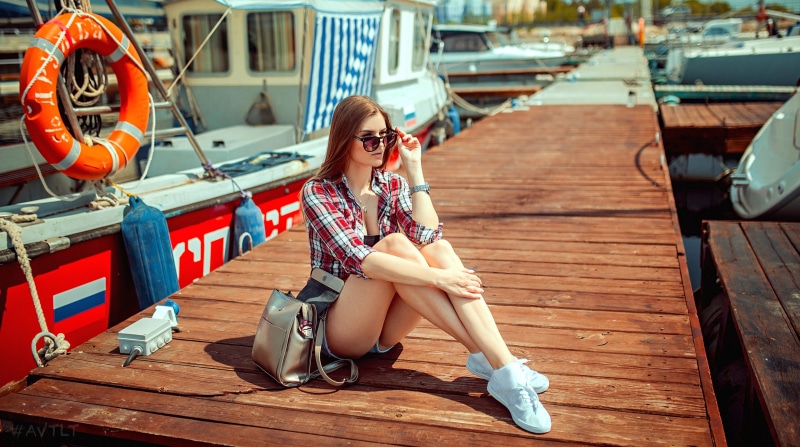 Woman in Plaid Shirt Sitting on Dock with Handbag