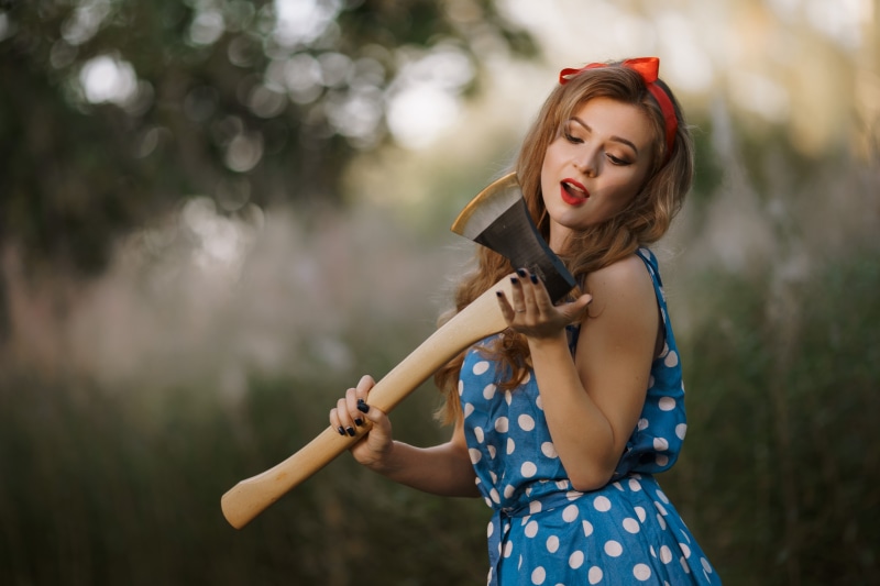 Woman in blue polka dot dress holding an axe
