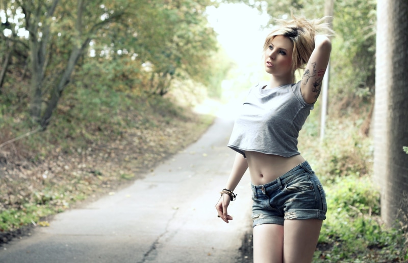 Blonde girl with tattoos in a crop top and shorts posing outdoors