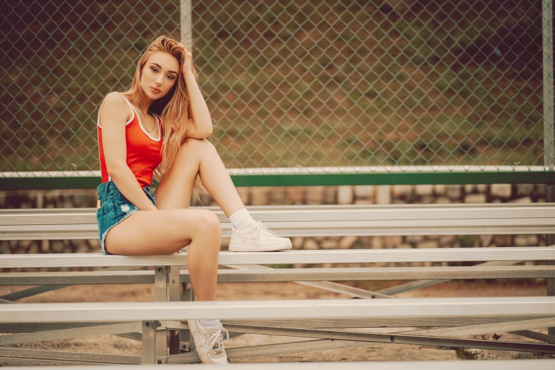 Redhead girl in singlet and shorts sitting on bleachers