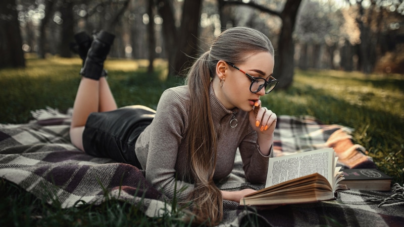 Woman wearing glasses reading a book in a park