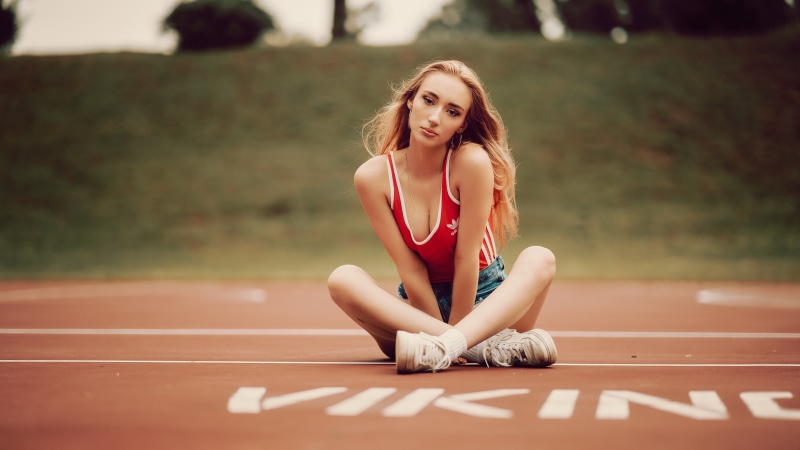 Woman in red singlet and denim shorts sitting on track