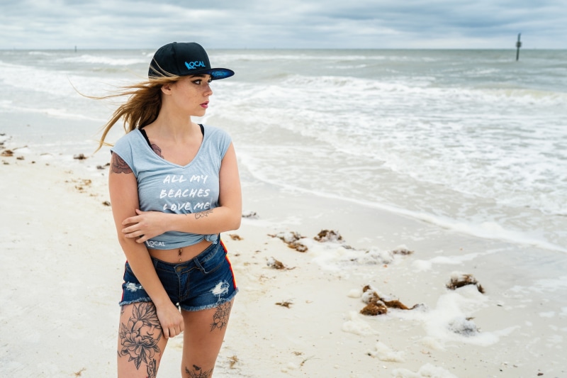 Woman with tattoos on a beach wearing a baseball cap and t-shirt