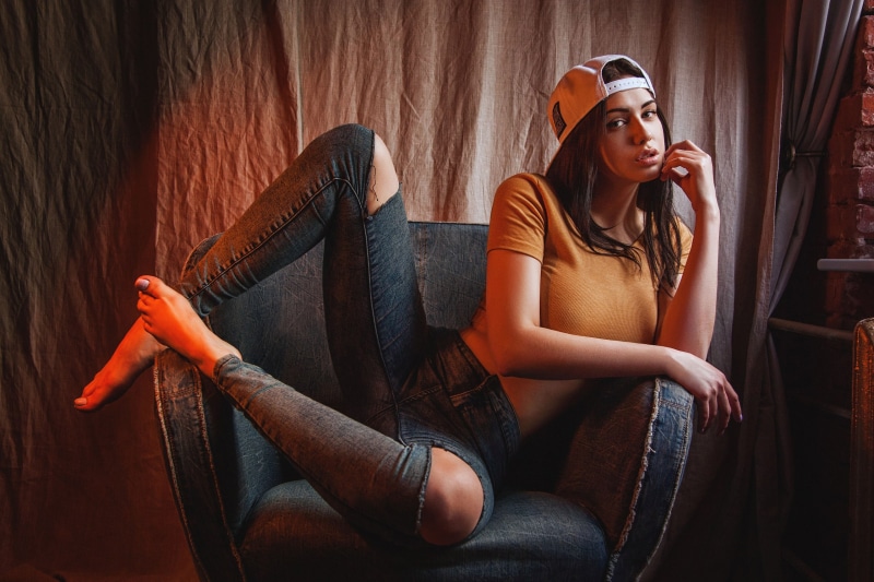 Woman in ripped jeans and baseball cap posing in armchair