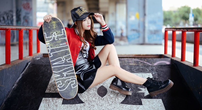 Asian woman with skateboard wearing baseball cap and boots