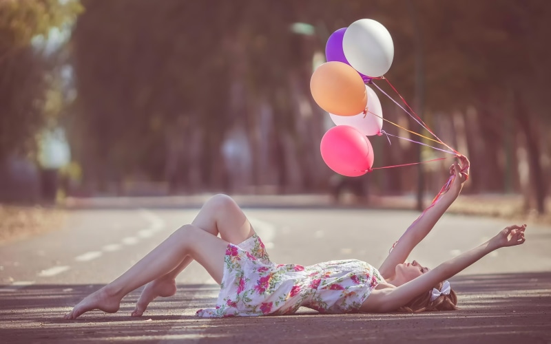 Woman lying on asphalt holding balloons