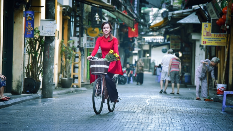 Woman in red dress riding bicycle with flowers in basket