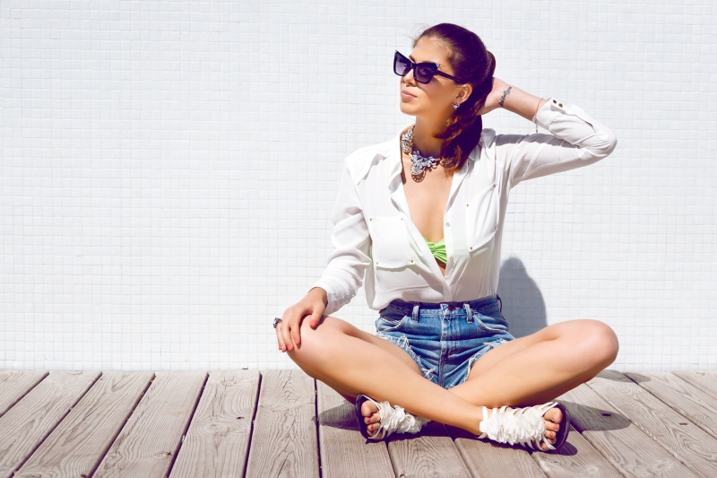 Brunette girl in sunglasses and white shirt sitting on wooden floor