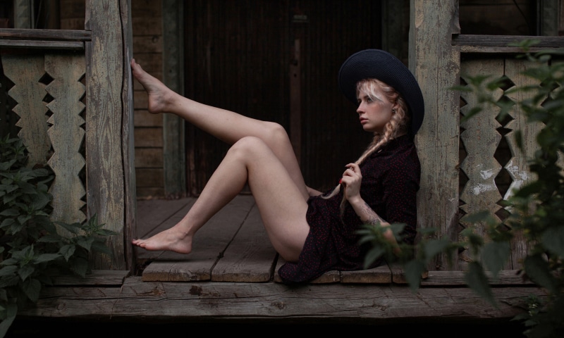 Blonde girl with hat and braid hair on wooden porch