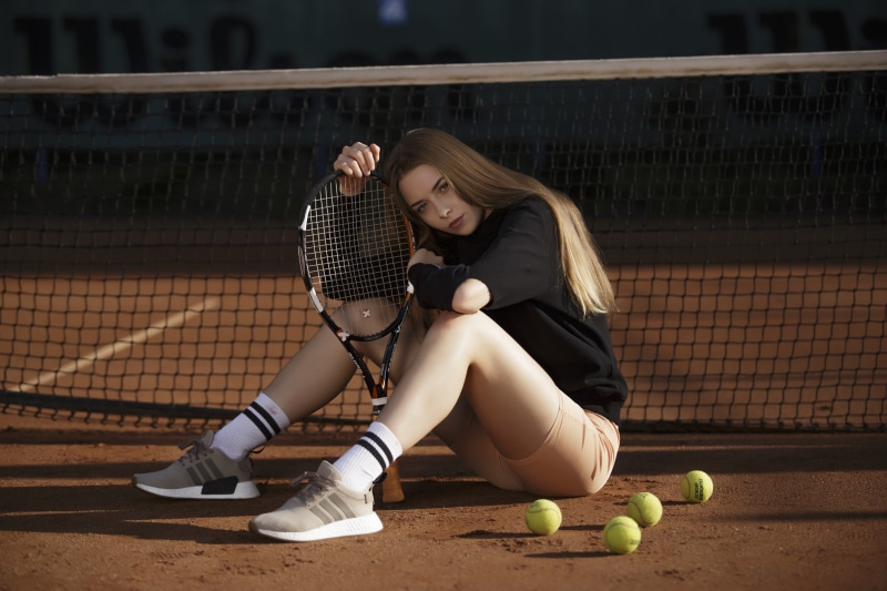 Young woman with tennis racket sitting on court