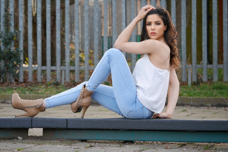 Brunette woman in jeans and white top posing outdoors
