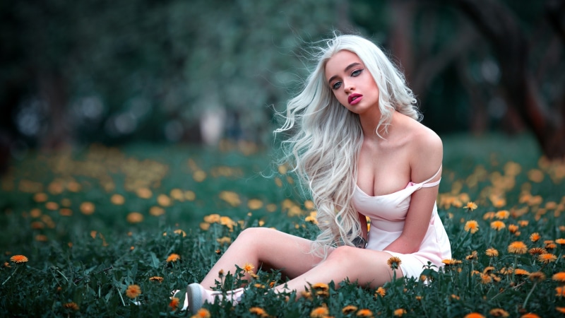 Blonde woman in a pink dress sitting in a field of flowers