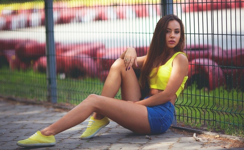 Woman in yellow top and blue shorts sitting by fence