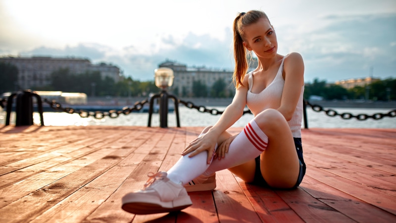 Woman in singlet and knee-high socks sitting on wooden pier