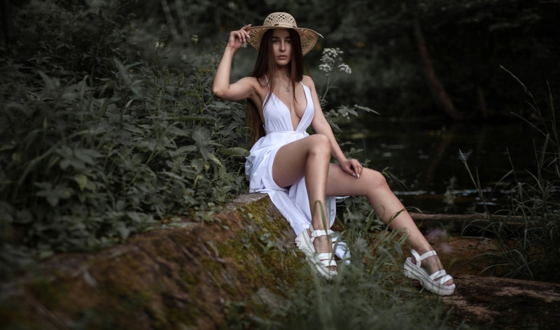Woman in white dress and hat sitting by water