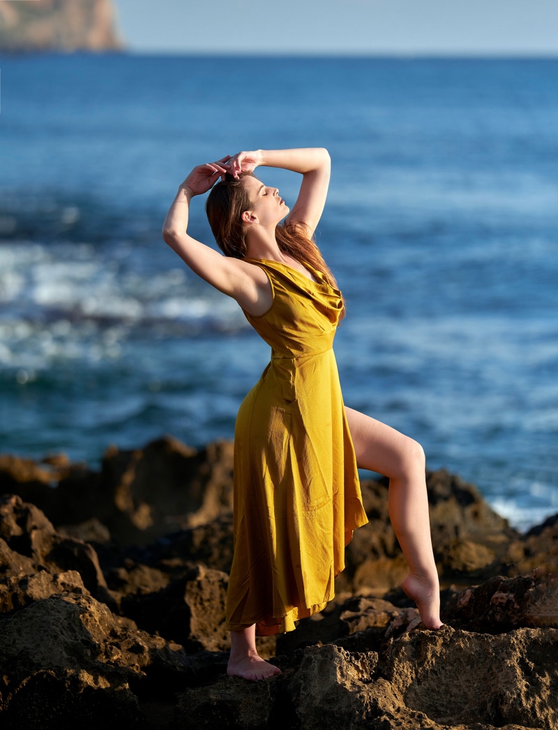 Woman in yellow dress posing on rocks by the sea