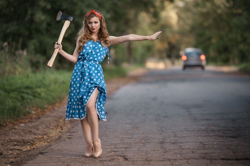 Woman with axe hitchhiking on a road