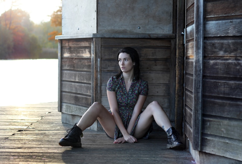 Emilia sitting on a wooden dock in a floral dress and boots