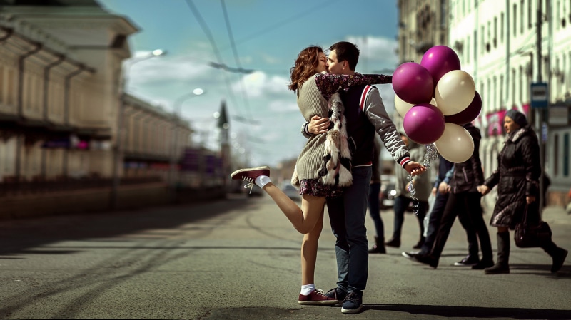 Couple kissing on street holding balloons