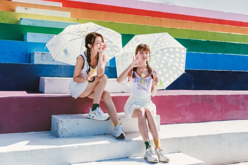 Two Asian girls with umbrellas sitting on colorful stairs